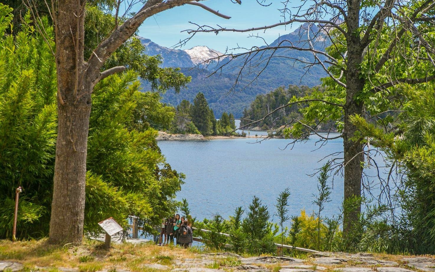 Lake Nahuel Huapi surrounded by forest on Victoria Island, with visitors walking nearby.