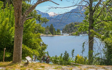 Lake Nahuel Huapi surrounded by forest on Victoria Island, with visitors walking nearby.