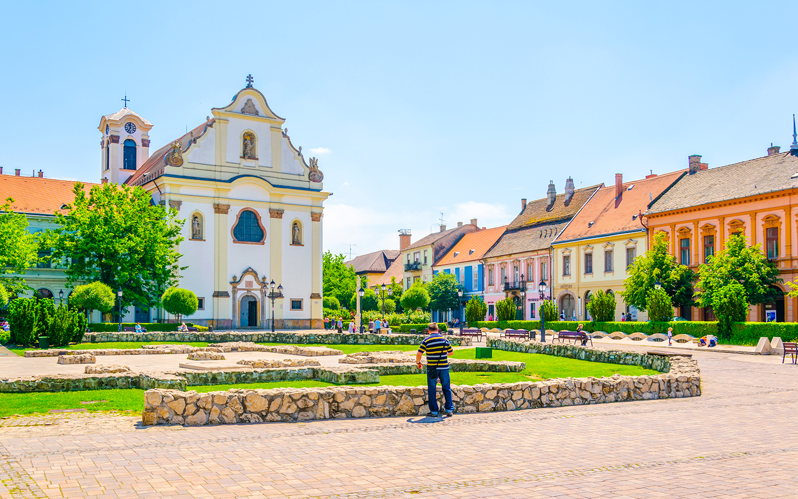Feherek Church in Vic, Hungary, with colorful historic buildings and a stone courtyard.
