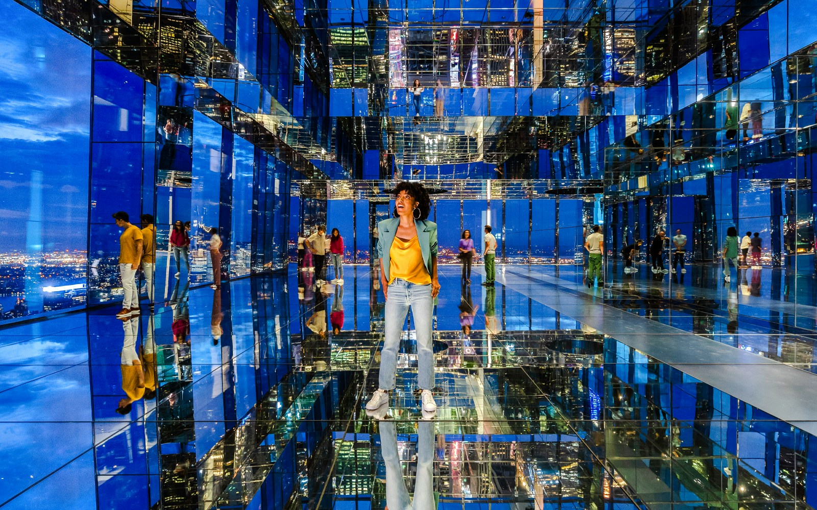 Guests enjoying night view from Summit One Vanderbilt, New York City skyline in background.