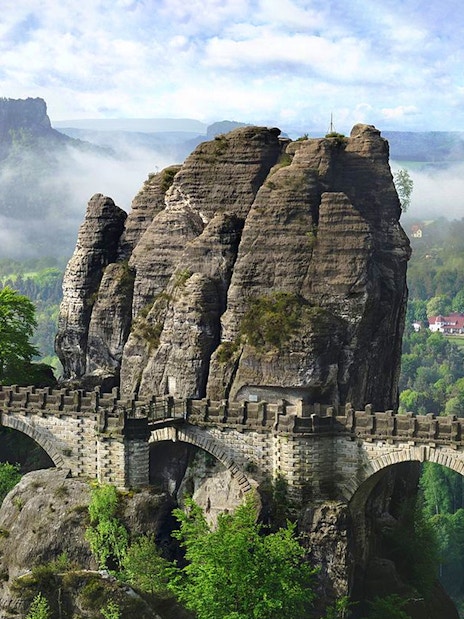 Bastei Bridge spanning rock formations in Saxon Switzerland, Germany, with lush greenery.