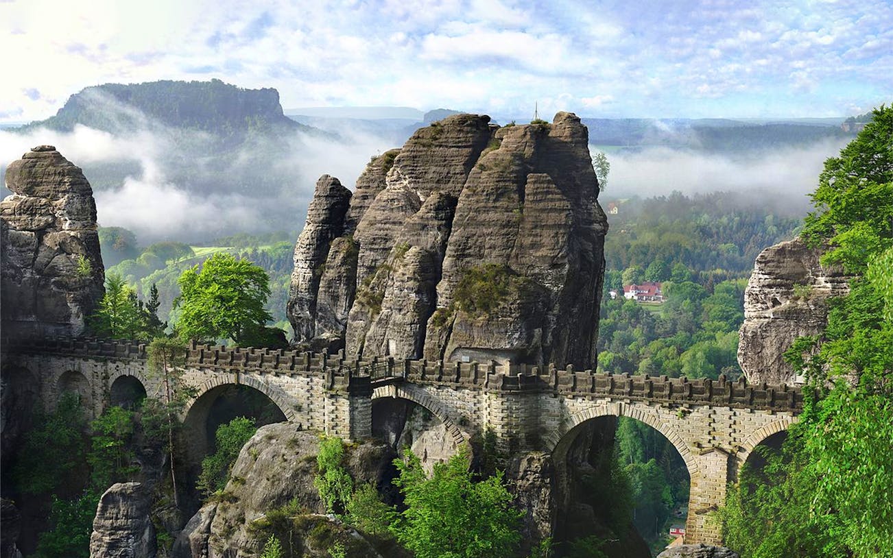 Bastei Bridge spanning rock formations in Saxon Switzerland, Germany, with lush greenery.