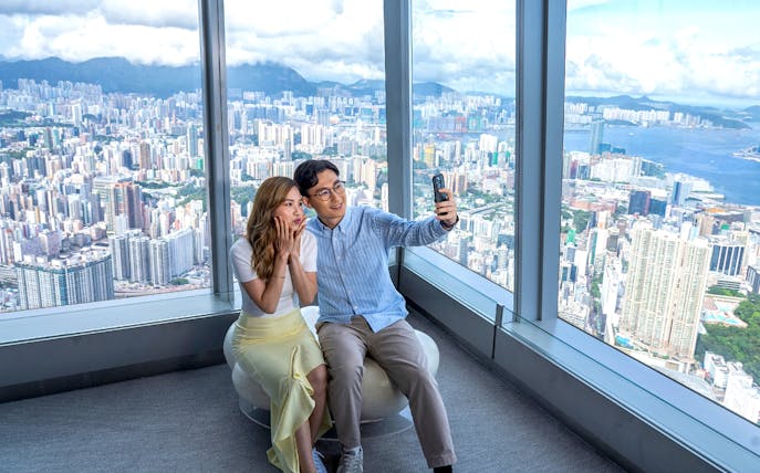 Couple taking a selfie at Sky100 Hong Kong Observation Deck with city skyline view.