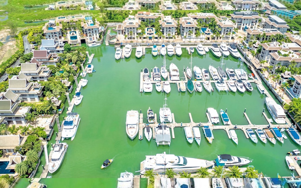 Marina with yachts and boats docked in a tropical resort setting, surrounded by lush greenery.