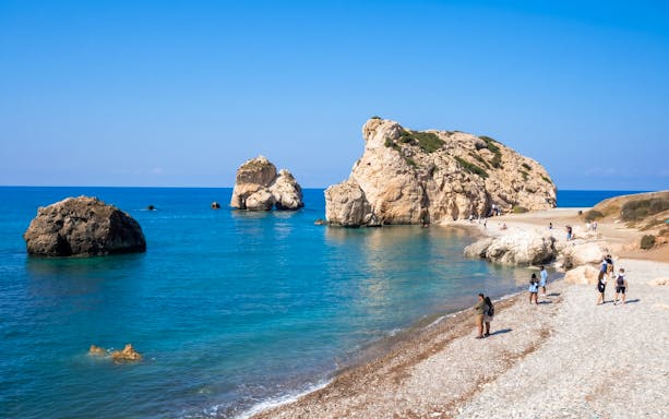 Visitors exploring Aphrodite's Rock on a sunny day in Paphos, Cyprus.