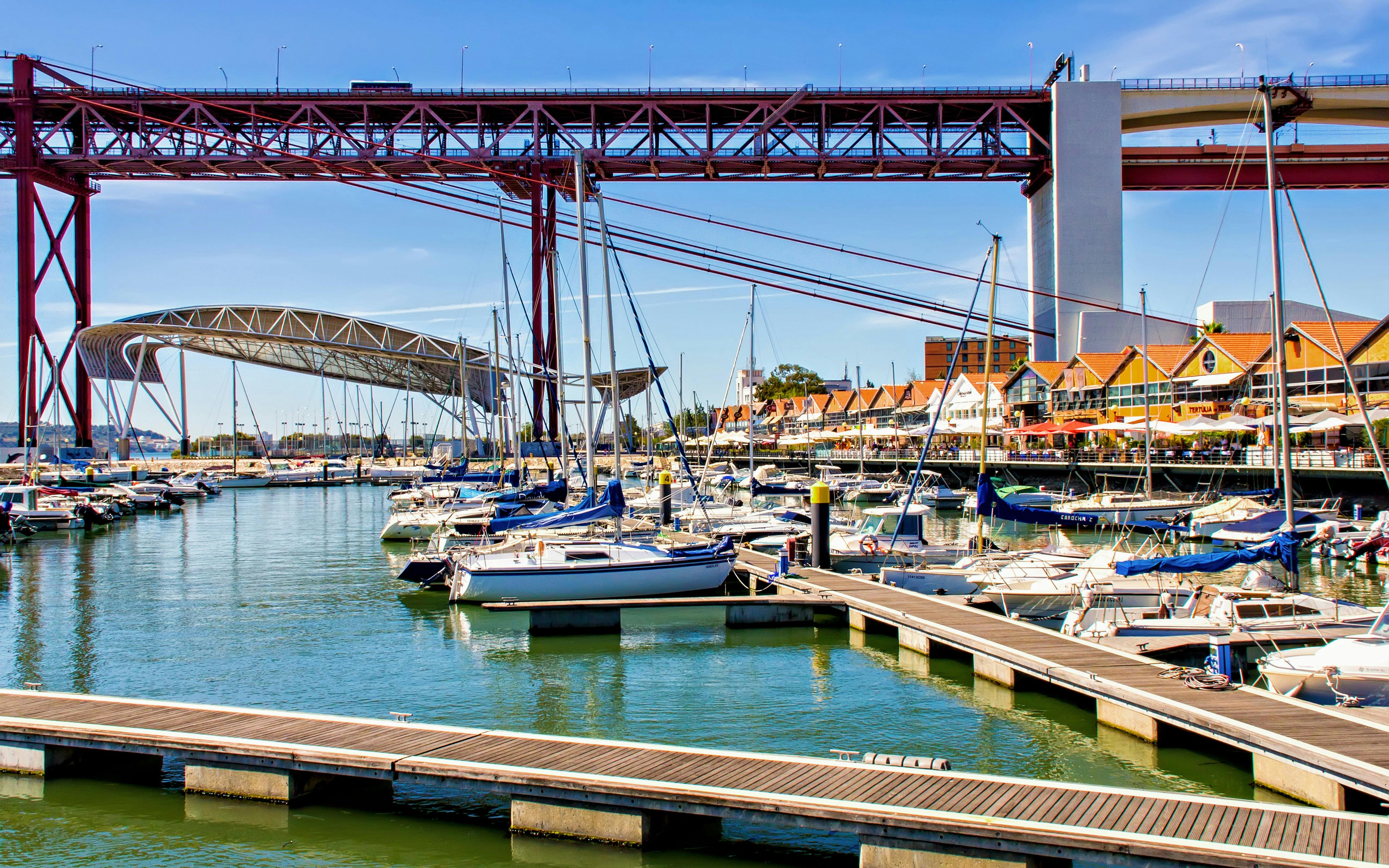 Sailboats docked at Santo Amaro Docks with 25 de Abril Bridge in Lisbon.
