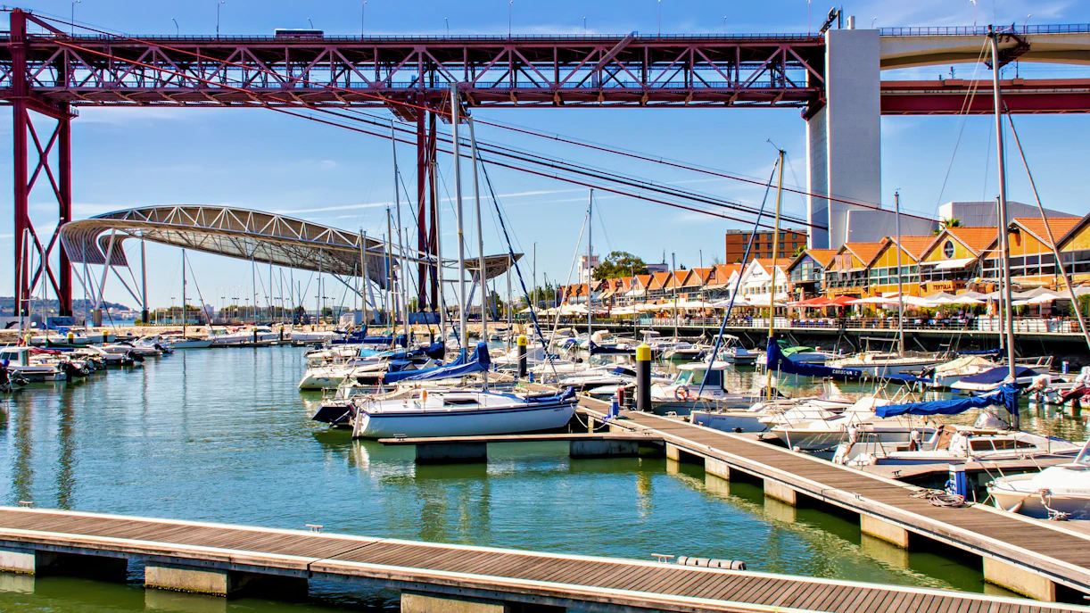Sailboats docked at Santo Amaro Docks with 25 de Abril Bridge in Lisbon.