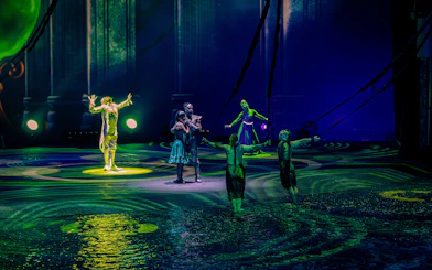 Performers on stage during La Perle show in Dubai, with vibrant lighting and water effects.