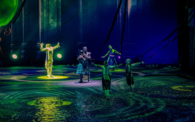 Performers on stage during La Perle show in Dubai, with vibrant lighting and water effects.