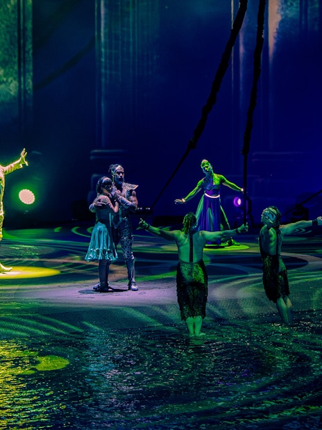 Performers on stage during La Perle show in Dubai, with vibrant lighting and water effects.
