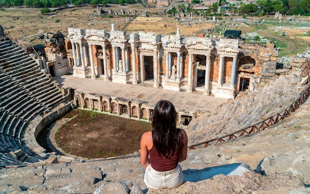 Woman sitting in Hierapolis ancient theater, Pamukkale, Turkey, overlooking the stage and ruins.