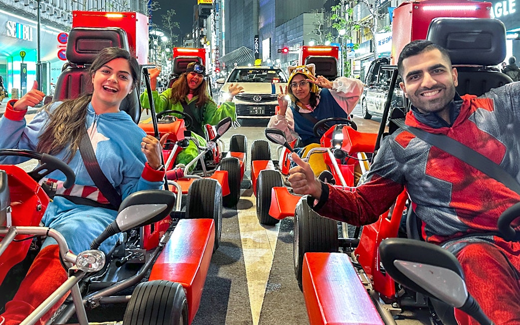 Group in costumes enjoying a go-kart ride on Shibuya streets at night.
