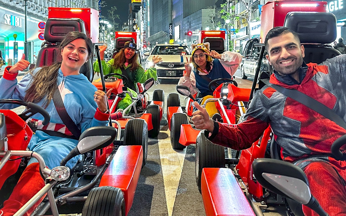 Group in costumes enjoying a go-kart ride on Shibuya streets at night.