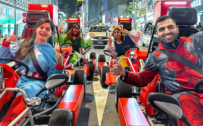 Group in costumes enjoying a go-kart ride on Shibuya streets at night.
