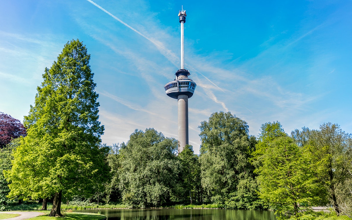 Public park with trees around a pond and Euromast tower in Rotterdam.