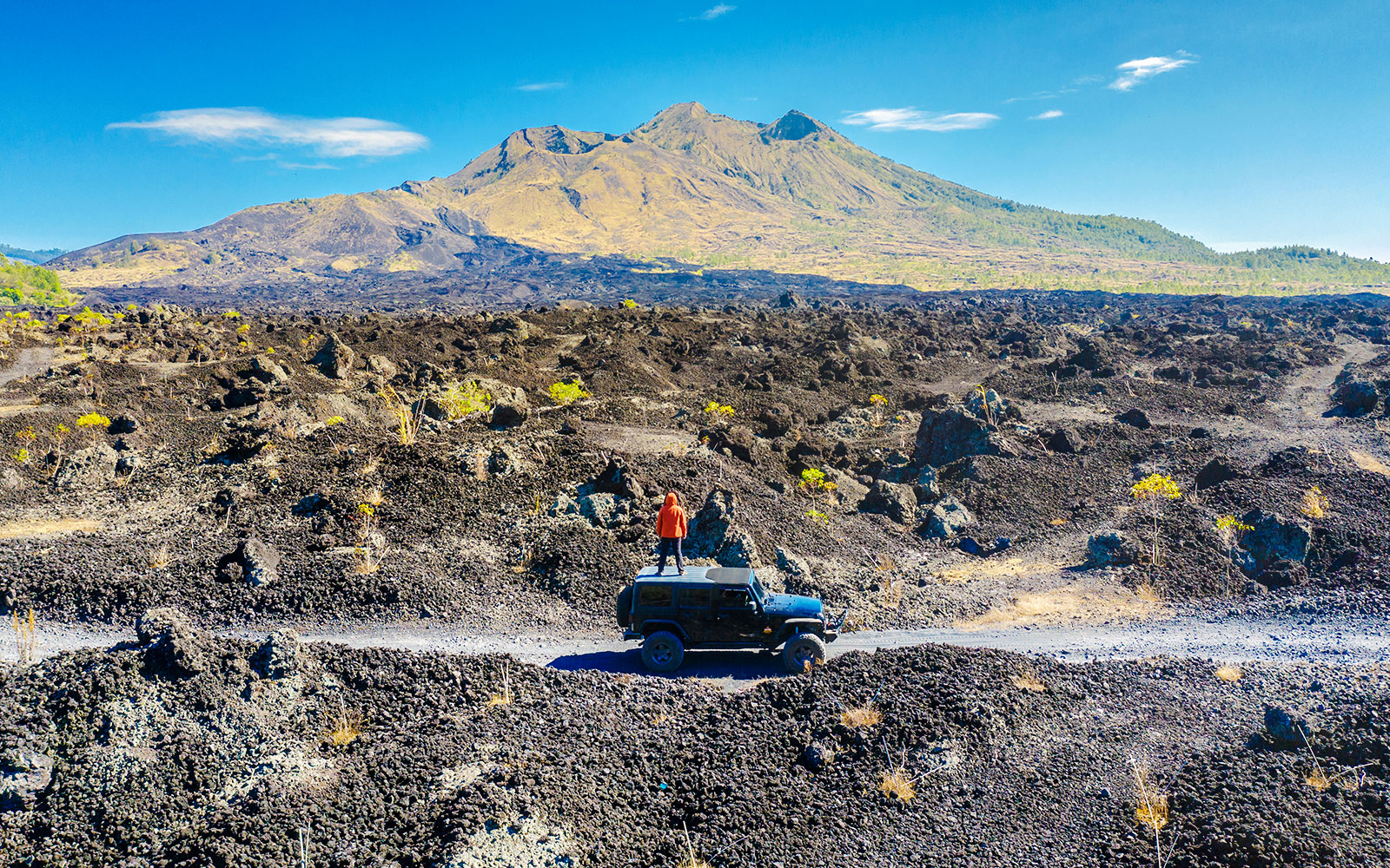 Man standing on a jeep enjoying Batur mountain view near black lava field.