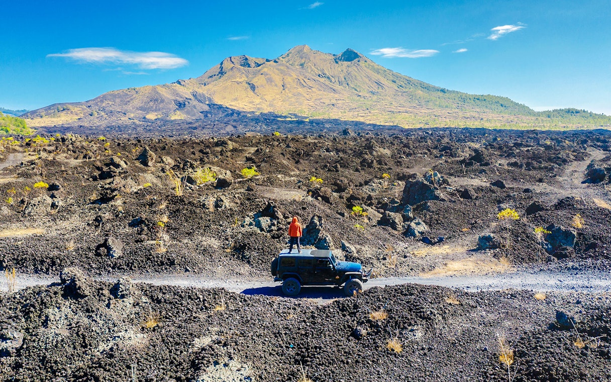 Man standing on a jeep enjoying Batur mountain view near black lava field.
