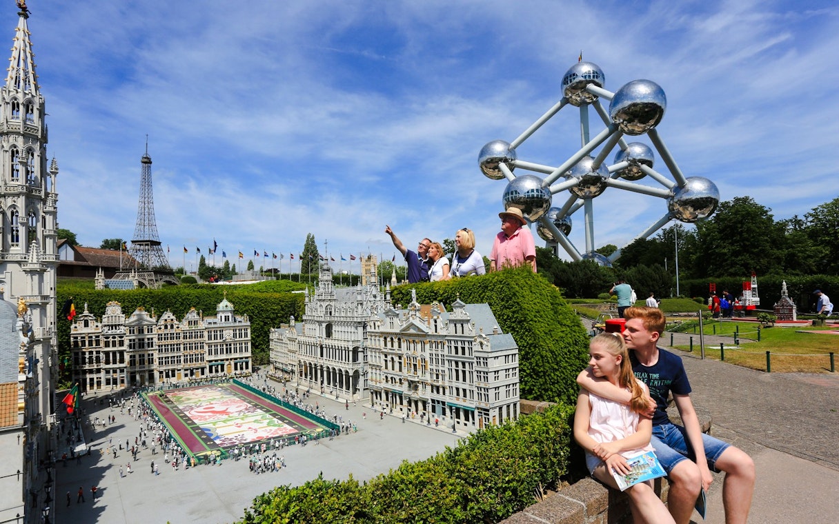 Tourists exploring Mini-Europe park with Atomium in Brussels.