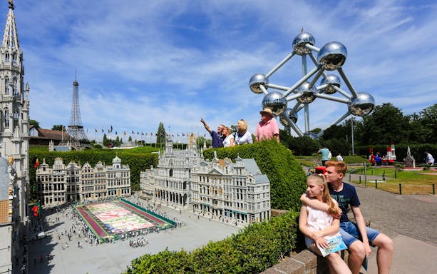 Tourists exploring Mini-Europe park with Atomium in Brussels.