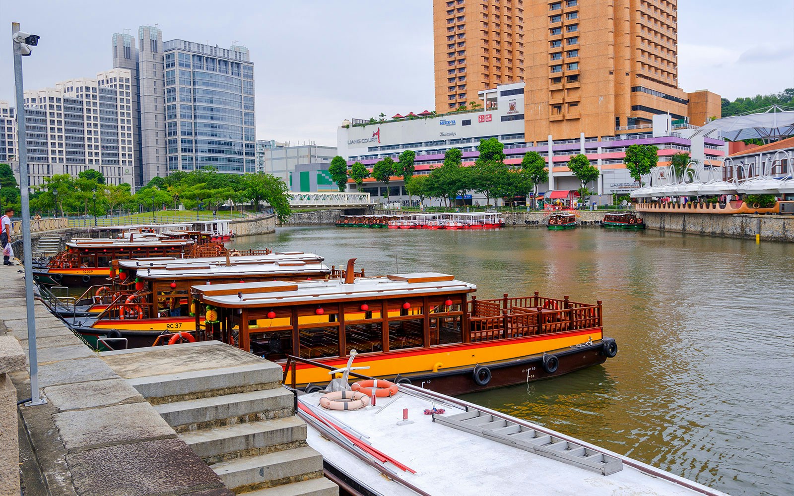 Traditional boats docked along the Singapore River with city buildings in the background.