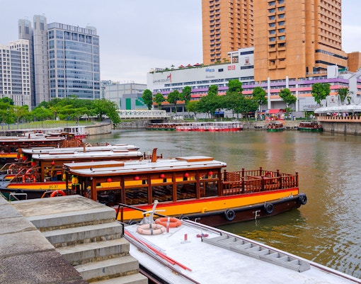 Singapore River Cruise boat passing under historic bridge with city skyline in background