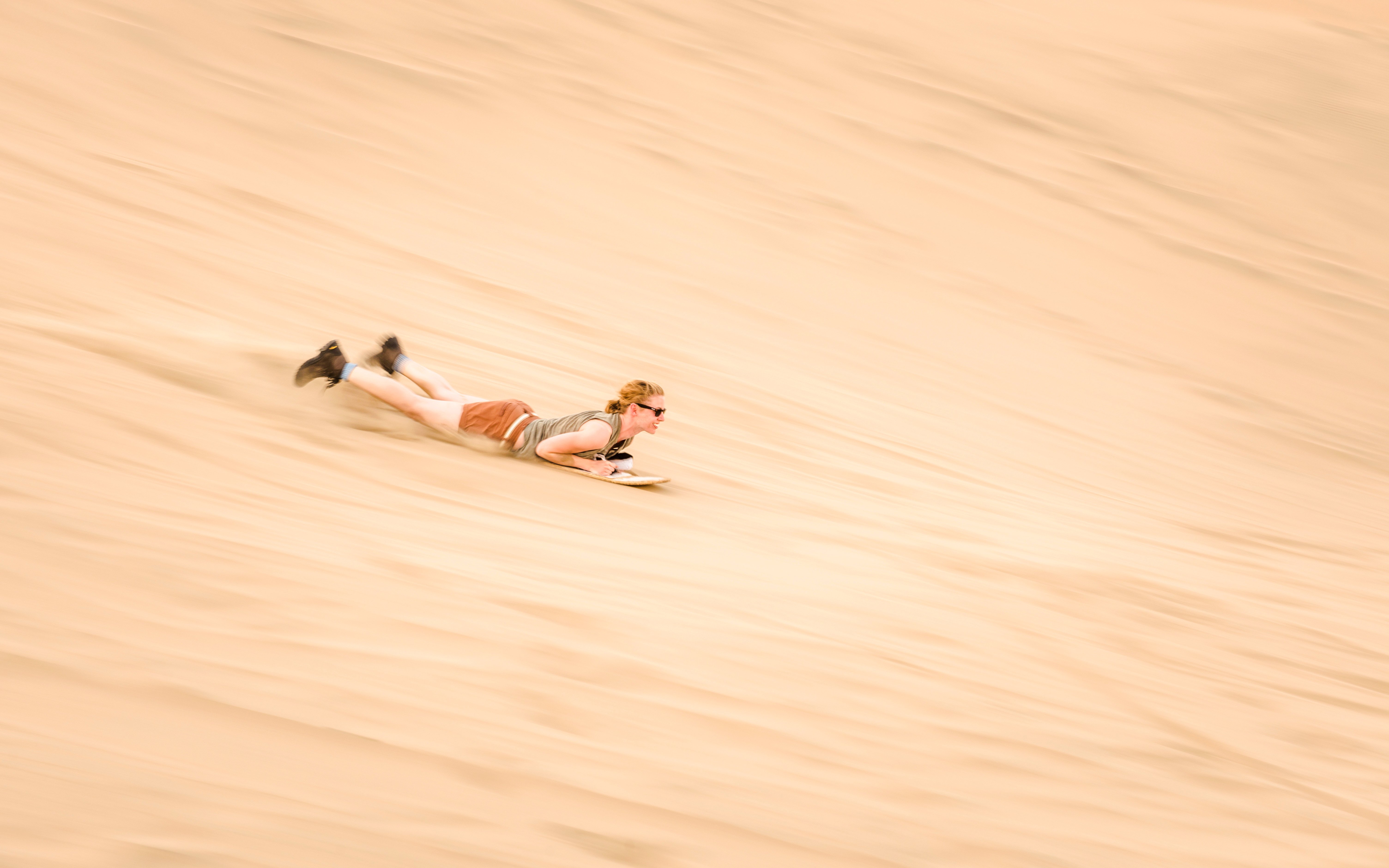 Person sandboarding down a dune in Doha desert, Qatar.