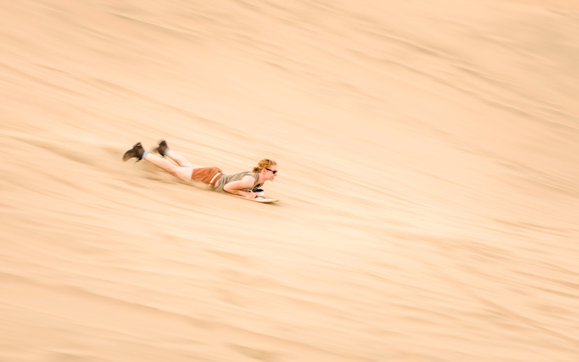 Person sandboarding down a dune in Doha desert, Qatar.