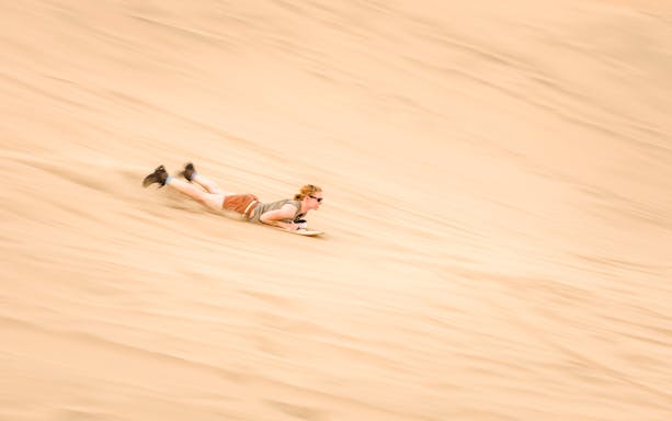 Person sandboarding down a dune in Doha desert, Qatar.
