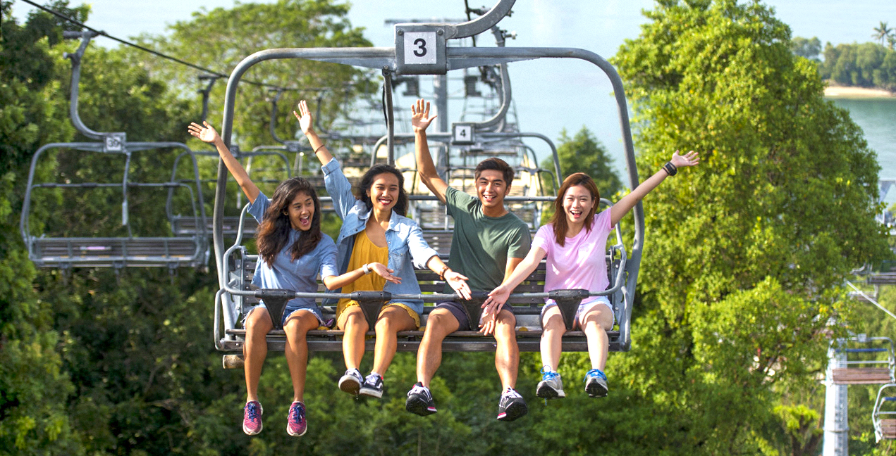 People riding a chairlift at Skyline Luge Singapore, surrounded by lush greenery.