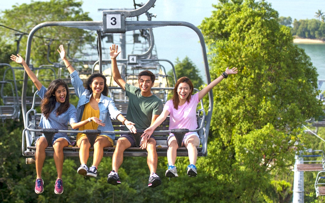 People riding a chairlift at Skyline Luge Singapore, surrounded by lush greenery.