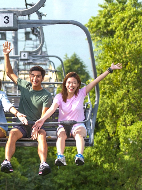 People riding a chairlift at Skyline Luge Singapore, surrounded by lush greenery.