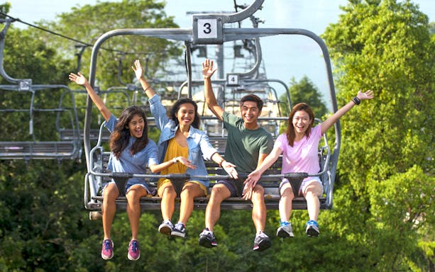 People riding a chairlift at Skyline Luge Singapore, surrounded by lush greenery.