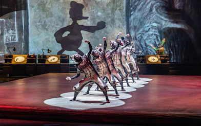 Performers in costume on stage with animated character shadow in "Drawn to Life" show.