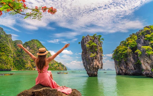 Tourist enjoying view of James Bond Island, Thailand, with limestone cliffs and clear water.