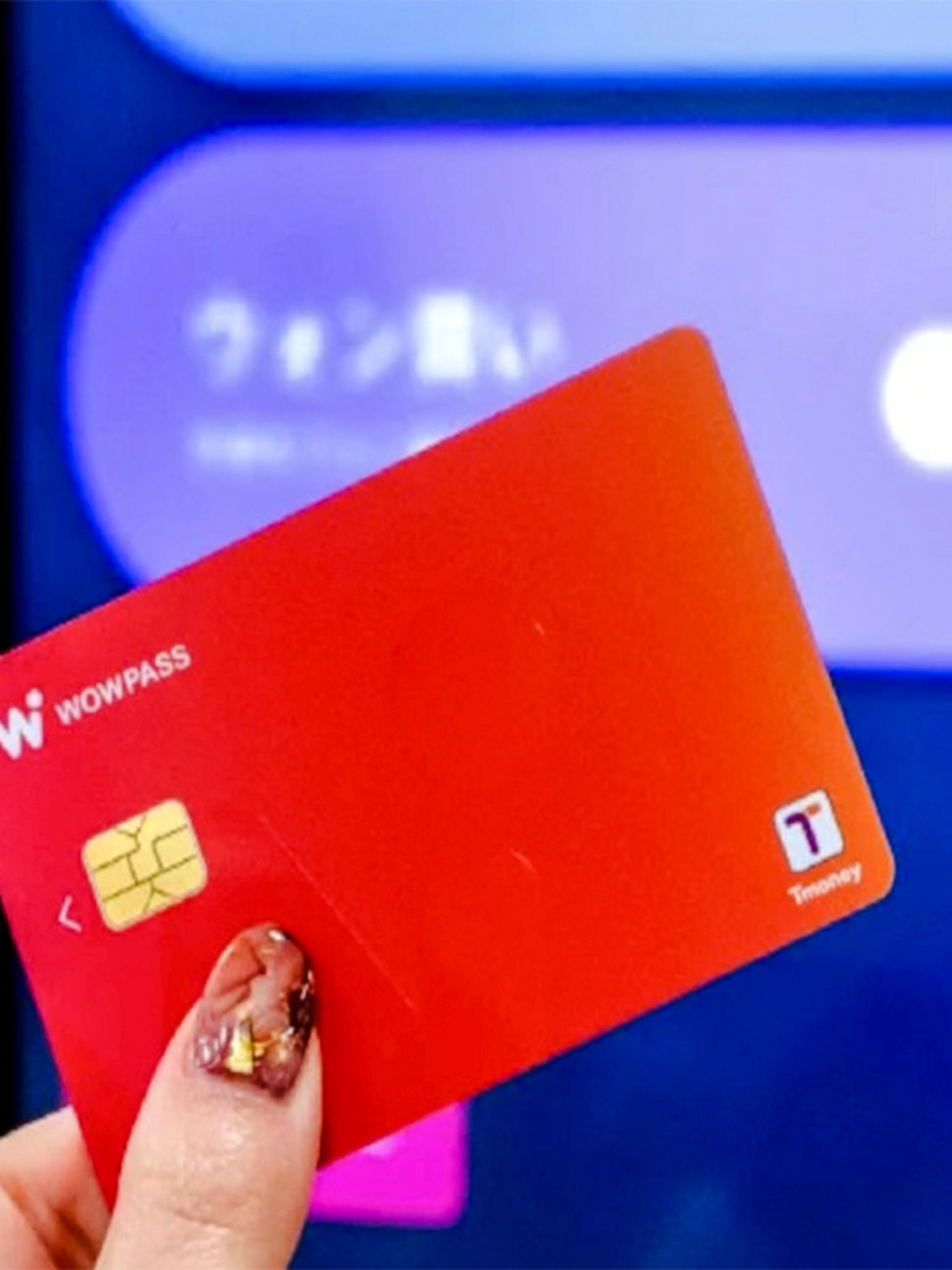 Hand holding a red Wow Pass card in front of a digital kiosk.