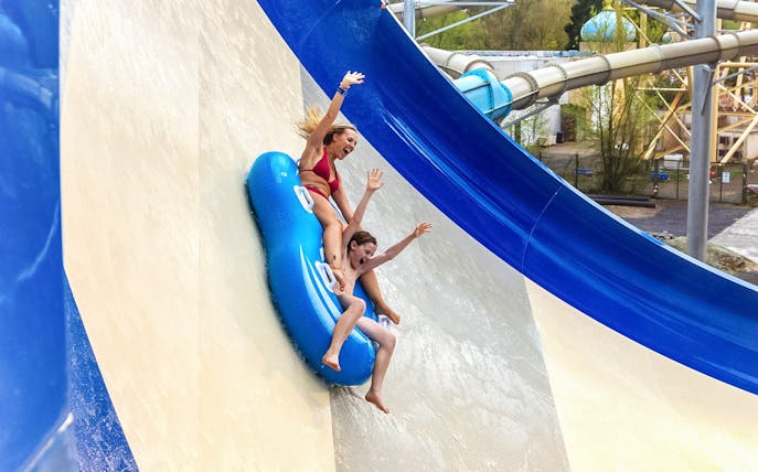 Tourists sliding down Waikiki slide at Aqualibi on a blue inflatable raft.