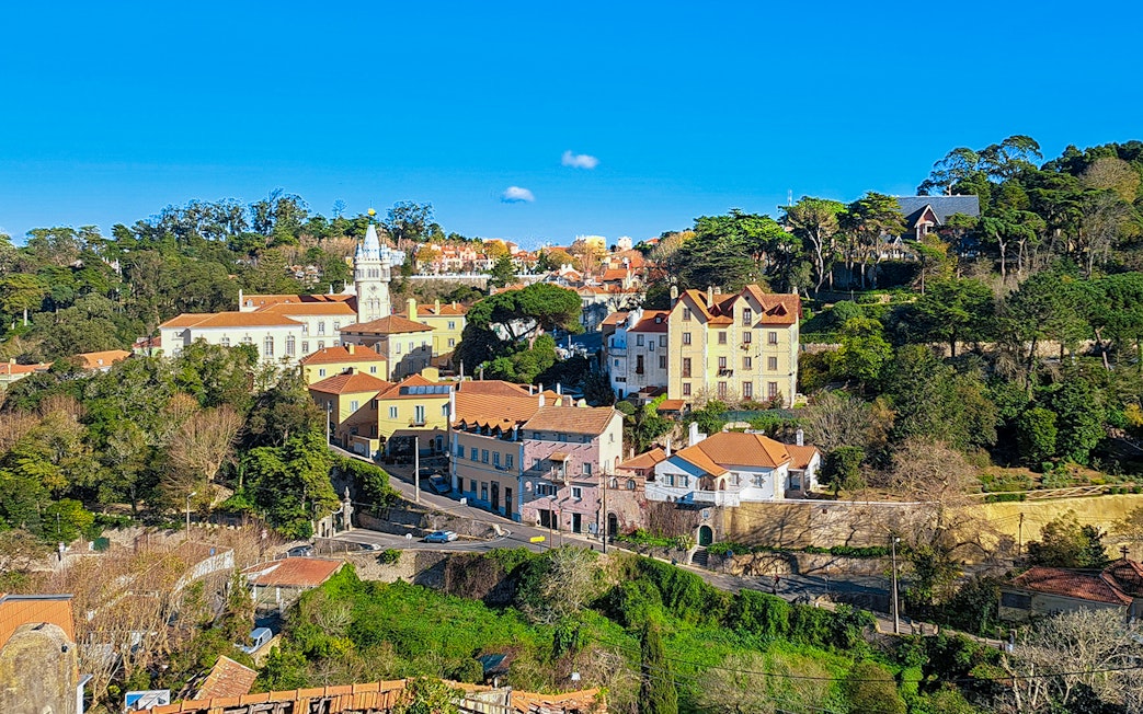 Sintra town road leading to Quinta da Regaleira, Portugal, with historic buildings and lush greenery.