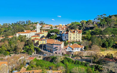 Sintra town road leading to Quinta da Regaleira, Portugal, with historic buildings and lush greenery.