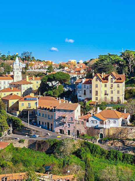 Sintra town road leading to Quinta da Regaleira, Portugal, with historic buildings and lush greenery.
