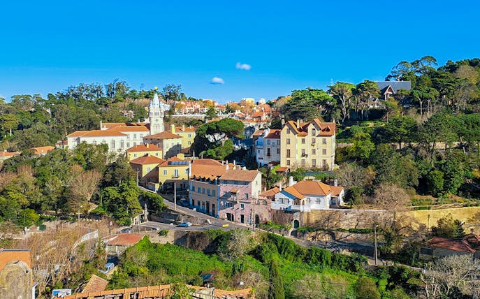 Sintra town road leading to Quinta da Regaleira, Portugal, with historic buildings and lush greenery.