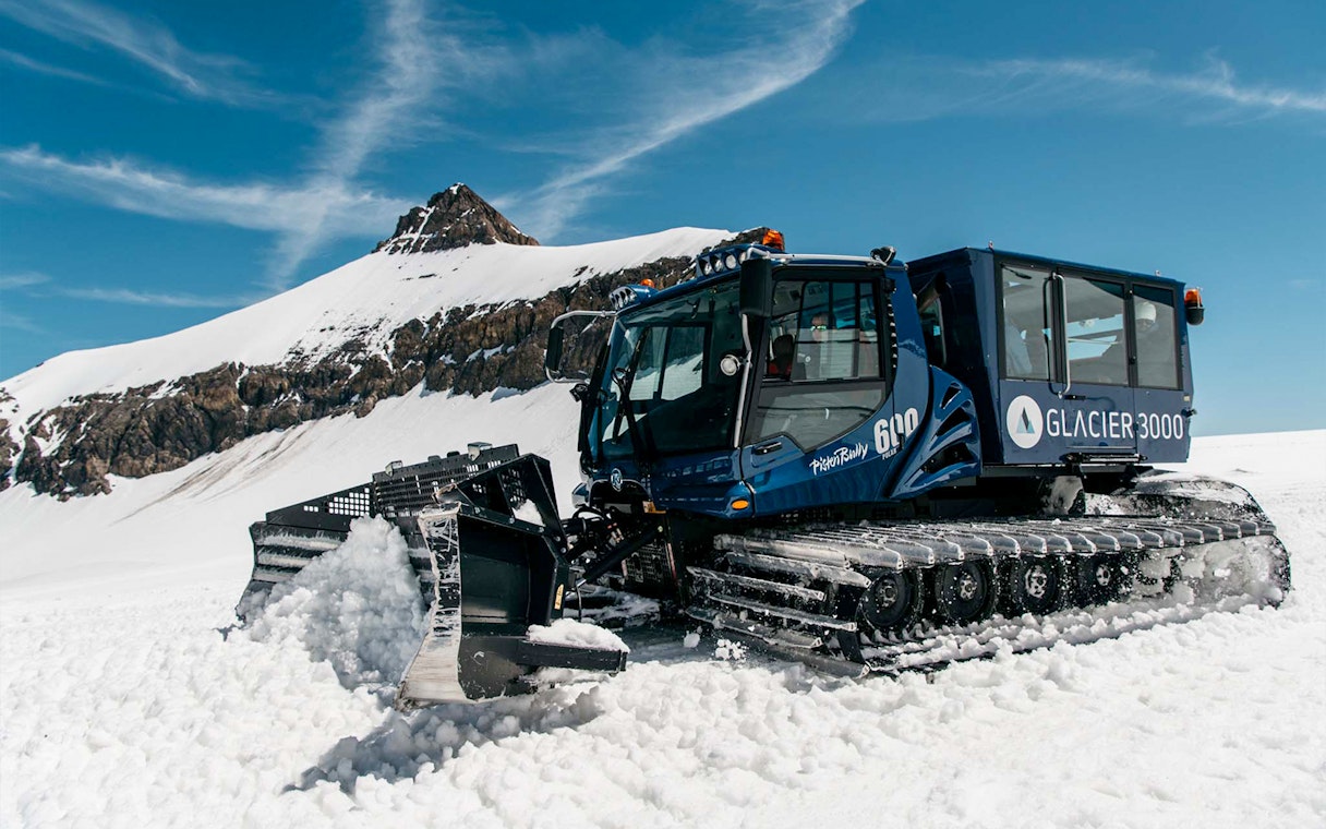 Snow groomer on Glacier 3000 in Les Diablerets, Switzerland, with snowy mountain backdrop.