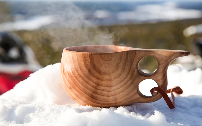 Steaming wooden cup on snow during snowmobile tour in Rovaniemi.