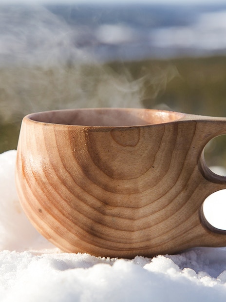 Steaming wooden cup on snow during snowmobile tour in Rovaniemi.