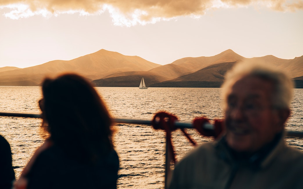 Sailboat on Lanzarote waters at sunset with tourists on deck.