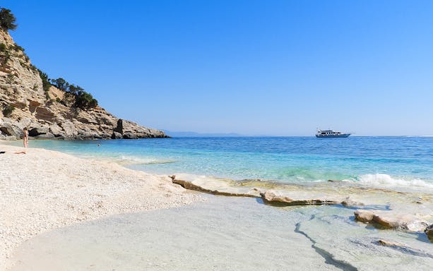 Boat on clear waters near rocky coastline, Costa di Baunei.
