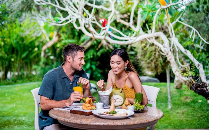 Couple dining outdoors at Bali Bird Park with tropical drinks and food.