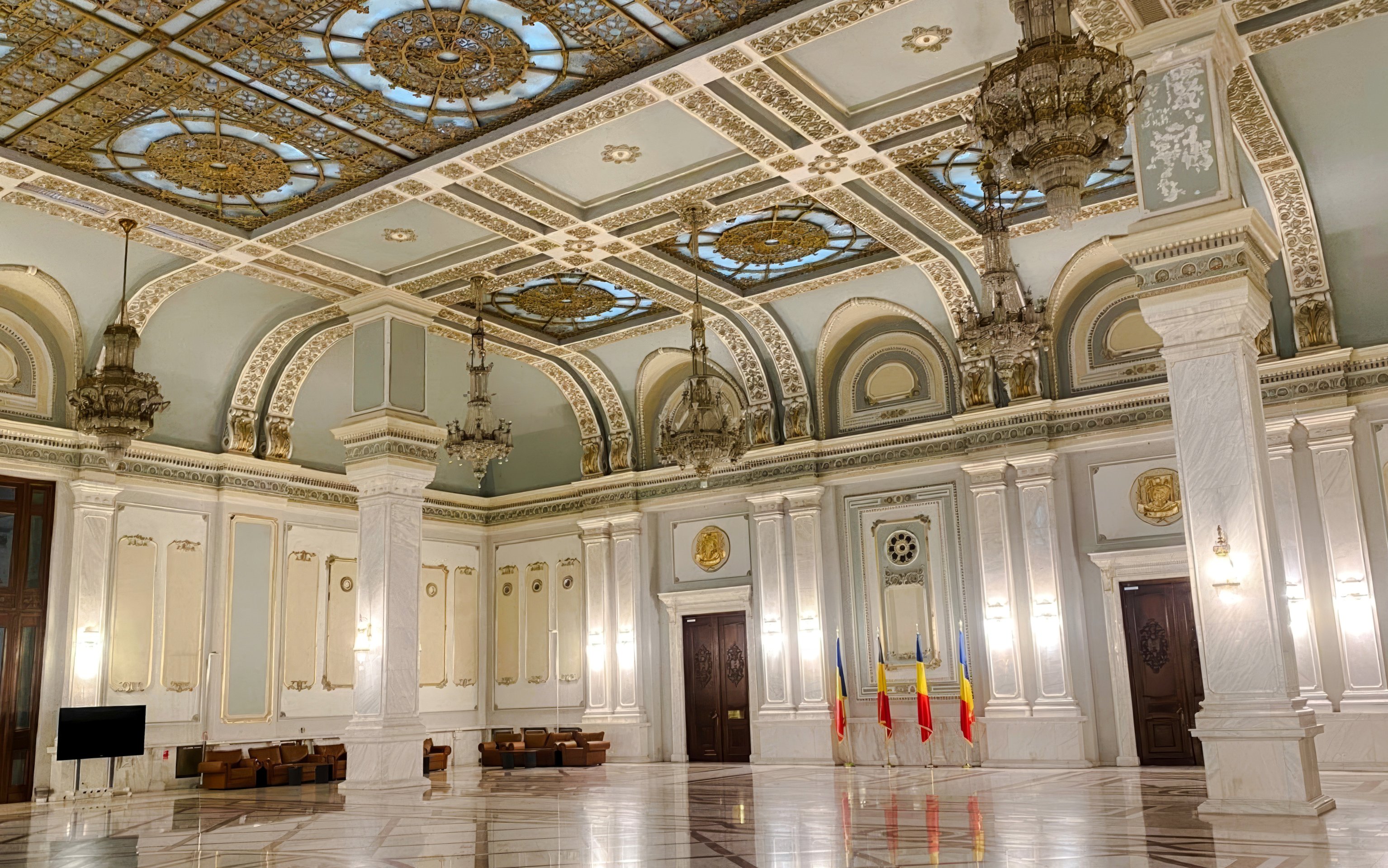 Interior view of ornate hall with chandeliers and Romanian flags inside Parliament of Romania.