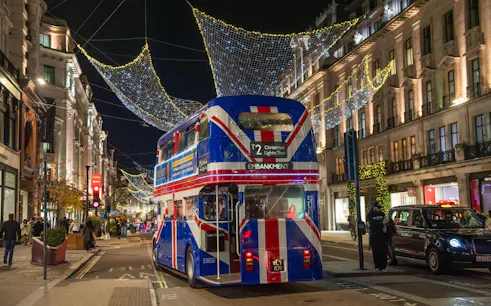 Double-decker bus on London street with Christmas lights overhead.
