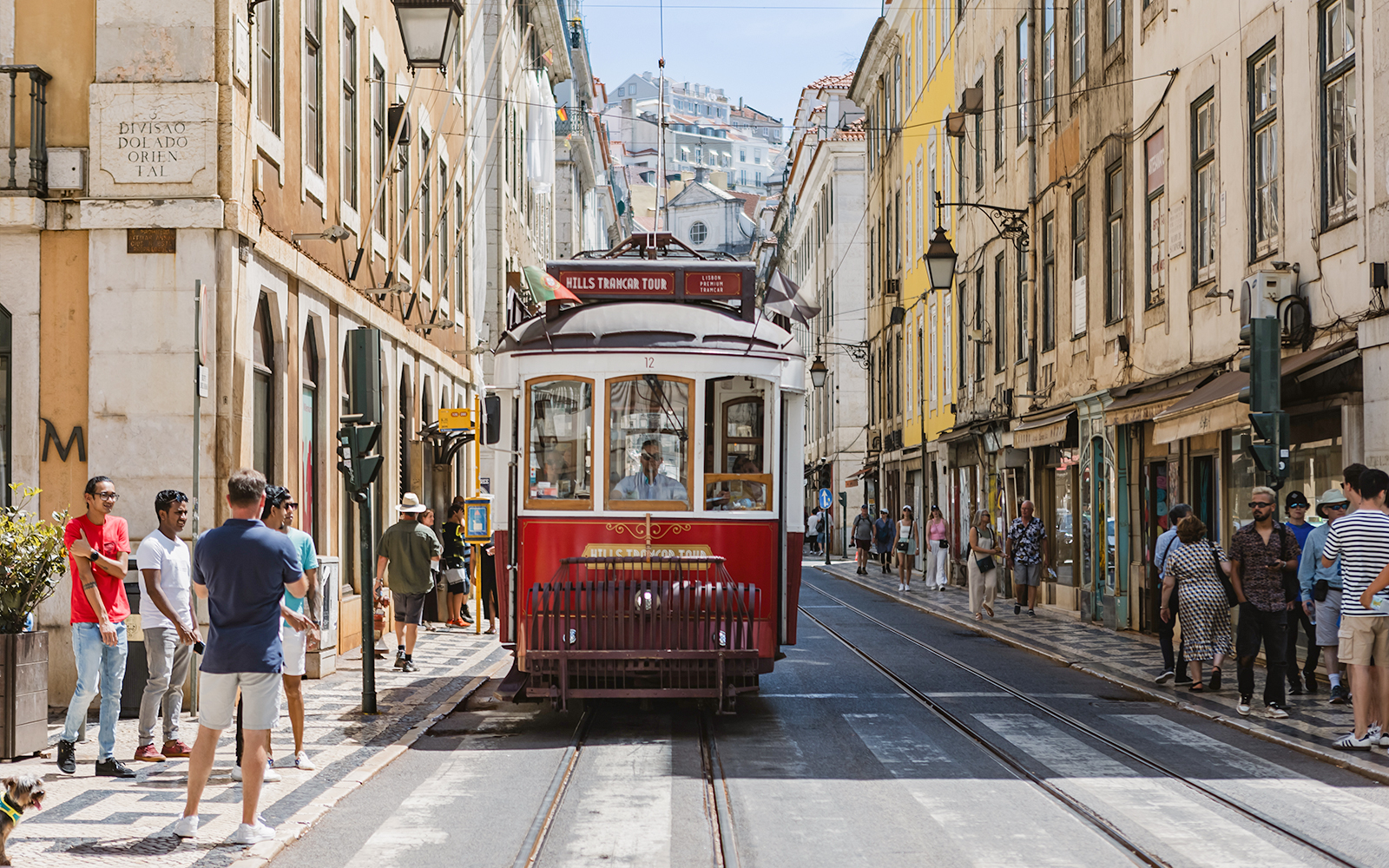 Lisbon tram on a city street with people walking nearby.