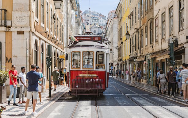 Lisbon tram on a city street with people walking nearby.